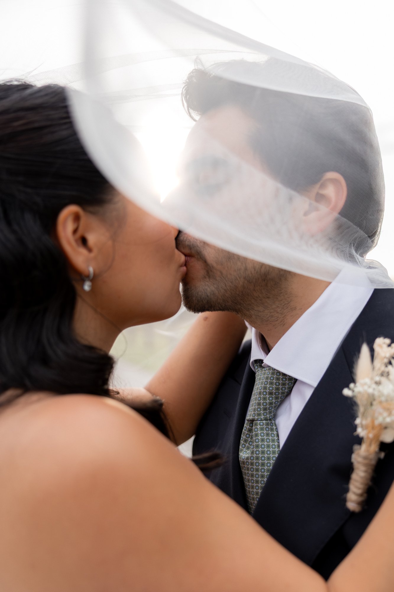 Un couple de mariés s’embrasse sous un voile